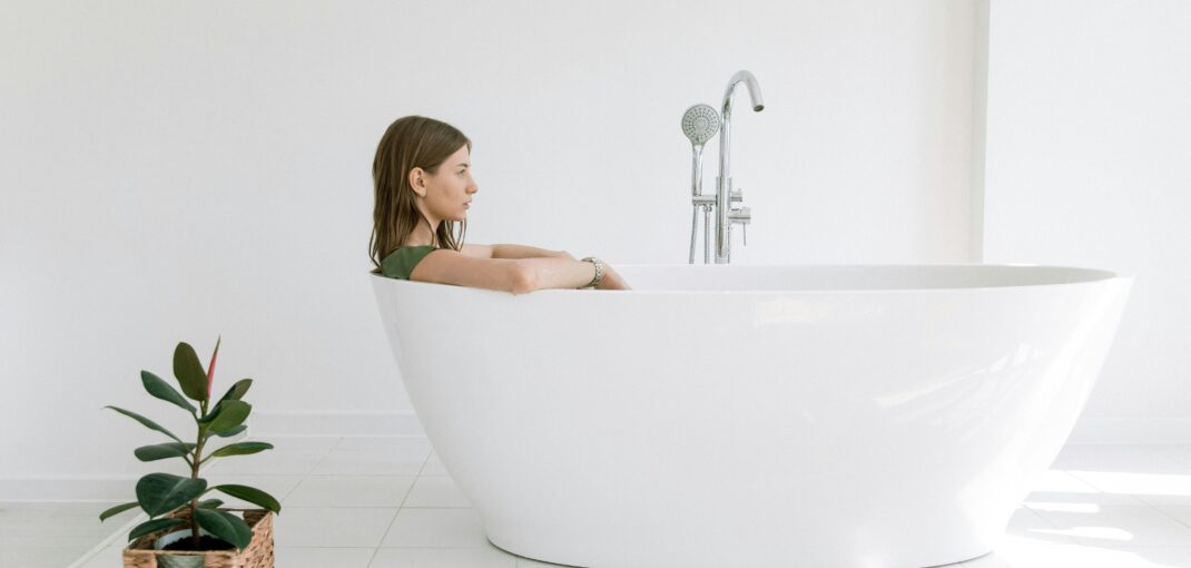 Woman enjoying a relaxing bath in a stylish white tub in a minimalist bathroom setting.