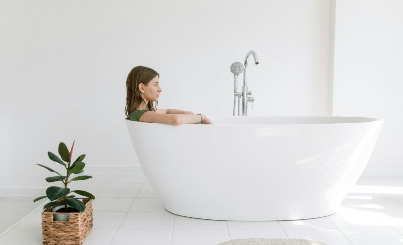 Woman enjoying a relaxing bath in a stylish white tub in a minimalist bathroom setting.